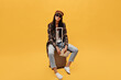 © Look! - Serious woman in brown beret and sunglasses sits on suit bag. Brunette girl in coat and jeans holds tickets on isolated yellow background.