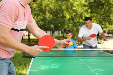 Wall Mural - Family with child playing ping pong in park, closeup