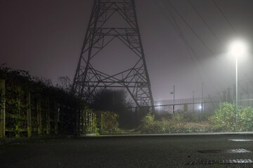 Wall Mural - An electricity pylon on an industrial estate back lighted on a foggy winters night.