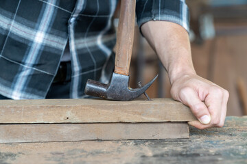 Male carpenter using hammer remove nail from wooden board at the carpentry workshop. Joiner working with hammer remove nails on wooden plank