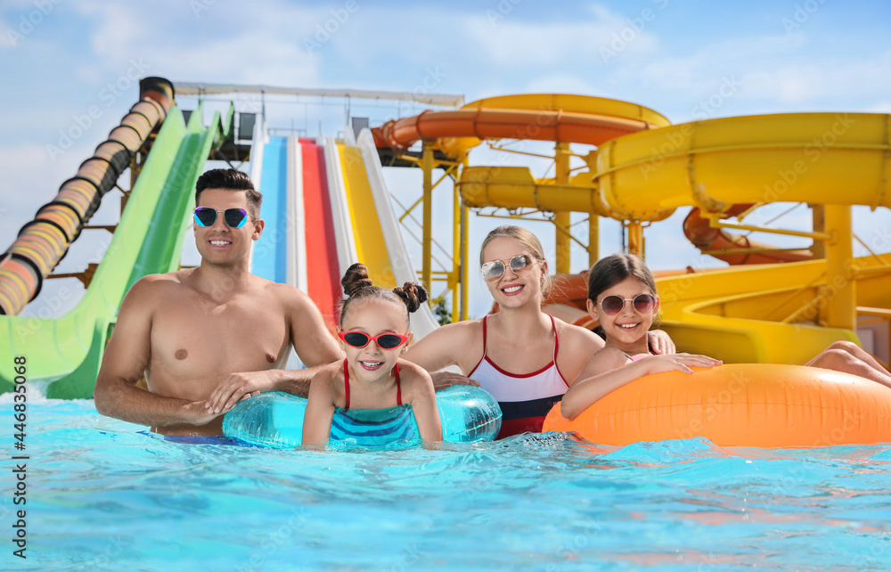 Happy family with inflatable rings in swimming pool at water park - obrazy, fototapety, plakaty 