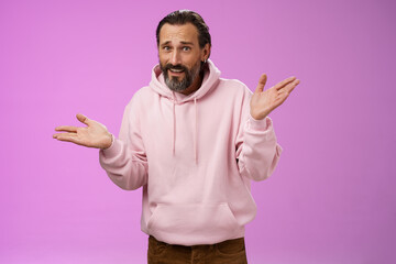 So what bite me. Portrait ignorant careless cool stylish mature bearded man earring pink hoodie shrugging hands sideways mocking being rude standing pissed unwilling help standing purple background