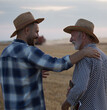 © Budimir Jevtic - Young farmer with hand on shoulder of elderly farmer talking smiling in field.