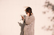 © Cavan Images - Side view of happy woman using smart phone while standing against wall