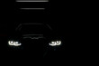 © Nischaporn - Unclear shape of front view sport car with headlights on dark background, Concept car concept, secret, new model car launch