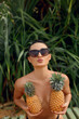 © verona_studio - Young beautiful girl posing on the tropical background , holding pineapples in hands.  Woman with bronze tan in bikini. Covering her breast with pineapples