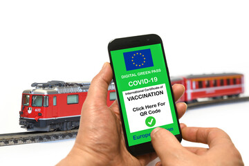 Wall Mural - The digital green pass of the European Union with the QR code on smartphone held by the hand with the model train in the background. Safe travel concept during the Coronavirus and the Green pass