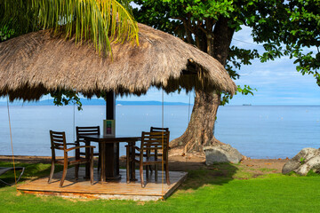 Beach resort facility empty closed for lockdown. Natural palm leaf gazebo on Philippine island. Seaside weekend resort with restaurant. Dining table under leaf roof with sea view. Travel ban in Asia