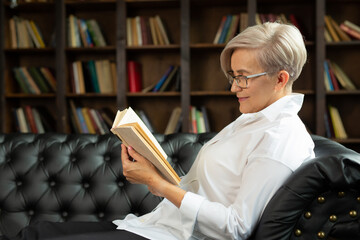 Wall Mural - beautiful aged woman reading a book indoors 