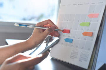 Event planner timetable agenda plan on organize schedule event. Business woman using mobile phone and taking note on calendar desk on office table