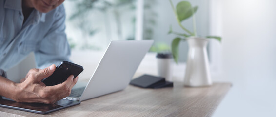 Close up of asian casual business man using mobile phone during working on laptop compter from home office with digital tablet on table, telecommuting, work from home concept