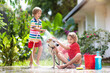 © famveldman - Kids wash dog in summer garden. Water hose fun.