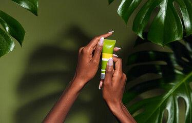 Wall Mural - natural skin care concept. photo of females hands holding a cream against green tropical plants