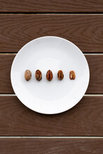 Pecans Symmetrically Arranged In A Row Some With A Shell And Others Without A Shell In A White Plate With A Wood Background.