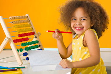 An african american student in a yellow dress laughs brightly behind a colored abacus in an elementary school