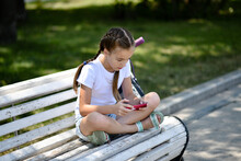 A Girl Plays On The Smartphone Sitting On A Bench
