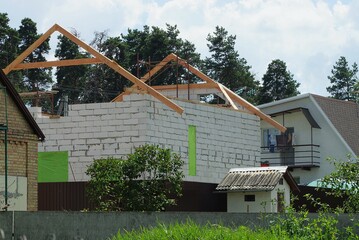 Sticker - white private brick house with an unfinished roof with brown wooden formwork on the street against a background of green trees and sky