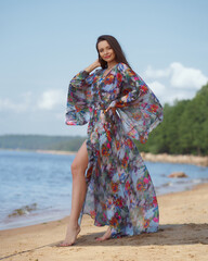 Wall Mural - Elegant woman in colorful tunic standing and posing at sandy beach on s ummer sunny day.