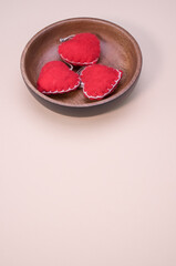 Canvas Print - Vertical shot of small red sewn hearts on a wooden bowl isolated on light pink background