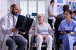 © DC Studio - Specialist doctor looking at patient x-ray explaining diagnosis to nurse in hospital office area. Handicapped elderly woman in wheelchair waiting for medical examination against virus disease