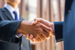 © Acronym - Handshake close-up. Businessman and his colleague are shaking hands in front of modern office building. Financial investors outdoor. Banking and business.