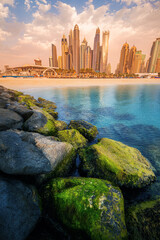 Wall Mural - Majestic rocks breakwaters in the foreground with the azure waters of the Persian Gulf and colorful skyscrapers in the Marina and JBR bay area in Dubai