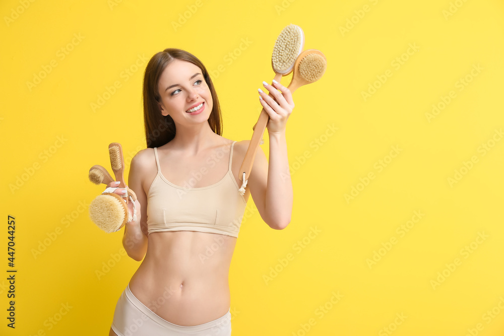Beautiful young woman with massage brushes on color background