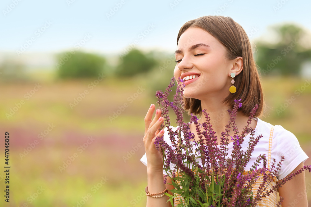 Beautiful young woman with summer flowers in blooming field - obrazy, fototapety, plakaty 