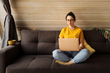 A girl in a yellow sweater is working at home using a laptop. A young girl works remotely during quarantine