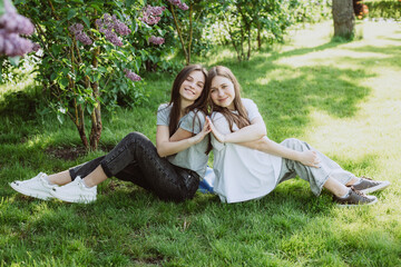 Wall Mural - Two young happy teenage girls are resting in the park on the green grass. Female friendship. Soft selective focus.