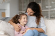 © fizkes - Smiling young Latino mom and teen daughter relax on sofa at home have fun cuddling tickling. Happy Hispanic mother and teenage girl child rest on couch enjoy family lazy leisure weekend together.