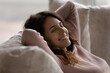 © fizkes - Smiling young Hispanic woman lying resting on couch at home relieve negative emotions breathe fresh ventilated condition air. Happy Latino female relax on sofa daydream sleep or take nap.