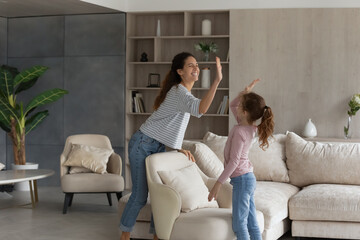 Overjoyed young Latino mother and little teen daughter give high five for well-done house work. Happy Hispanic mom and small teenage girl child celebrate finish job in new home. Rent concept.