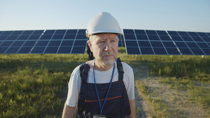 Adult man engineer technician working with modern solar battery panels on green sunny field. Futuristic technology innovation. Ecology and environment concept. Sunlight power. Eco-friendly system