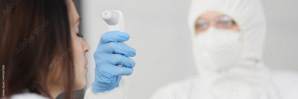 Doctor in protective suit and gloves measures temperature of person - obrazy, fototapety, plakaty 