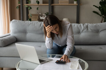 Desperate young woman sit on sofa at home calculates expenses feeling stressed about bank loan payments, lack of money, financial problems, thinking of unpaid taxes, bankruptcy, overdue bills concept