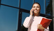 © Liubov Levytska - Smiling girl talking on mobile phone near university building. Happy student making a call on smartphone, holding study material, books from courses