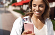 © Liubov Levytska - Portrait of happy attractive girl walking in city, girl standing on sunny street and reading message on mobile phone, using smartphone, cellular 4g internet