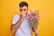 © WHstudio Leushin N - Seasoanl allergies and health concept. Unhappy man has runny nose and red swollen eyes uses handkerchief feels allergic to wild flowers poses against yellow background. Reaction on allergen.