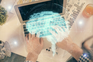 Double exposure of man's hands typing over computer keyboard and brain hologram drawing. Top view. Ai and data technology concept.