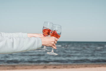 Wall Mural - Two glasses of rose wine in female's hands against the sky and seashore.