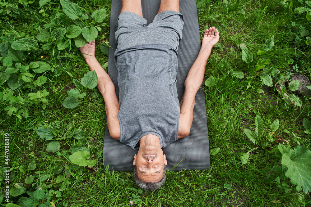 Man laying on sport mat, relaxing in savasana pose after exercising at the fresh air - obrazy, fototapety, plakaty 