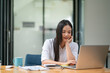 © Songsak C - A businesswoman puts her hand on her chin while using a laptop.