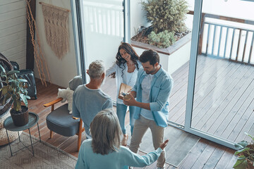 Wall Mural - Top view of happy senior parents meeting young couple inside the house