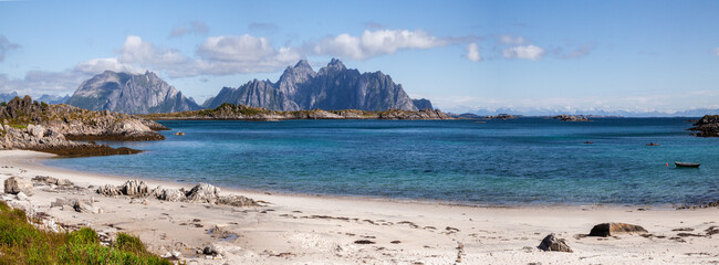 Beautiful picturesque Scandinavia panorama of a wide sandy beach on the shore of the blue calm bay of the Norwegian fjord with high rocky mountains on the horizon.