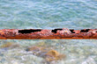 Remains of a rusted handrails on an abandoned waterfront on a blurred background of azure sea waves. Metal corrosion close-up.