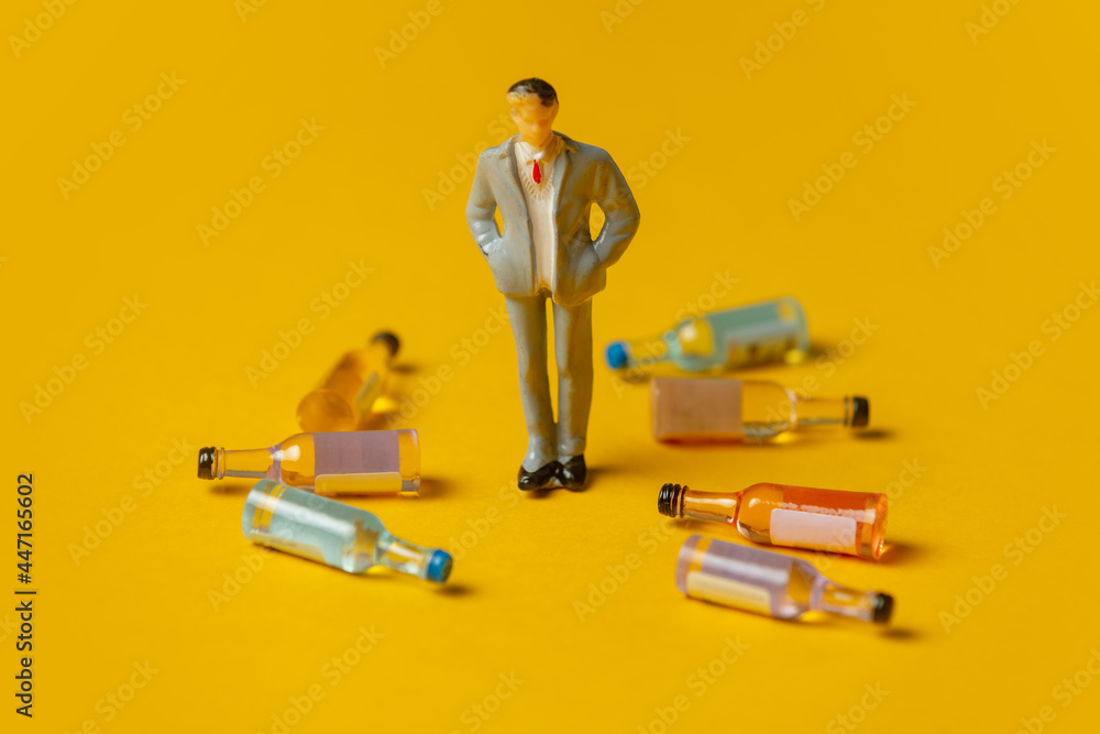 miniature figure of a man with alcohol bottles around him - obrazy, fototapety, plakaty 