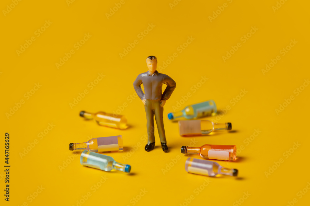 miniature figure of a man with alcohol bottles around him - obrazy, fototapety, plakaty 