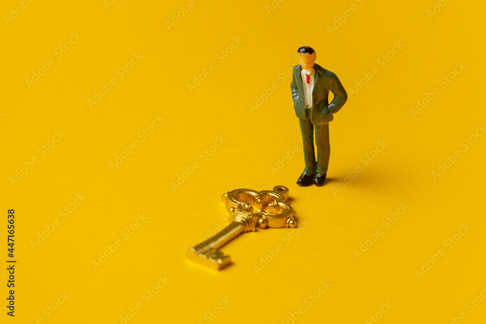 miniature figure of a man neat golden key on yellow background - obrazy, fototapety, plakaty 