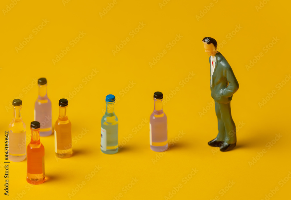 miniature figure of a man with alcohol bottles in front of him - obrazy, fototapety, plakaty 